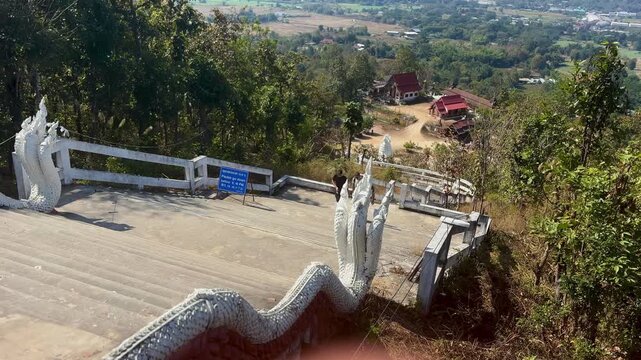 Naga lined staircase descending through hillside with temples red roof buildings and farmland overlooking the scenic valley in Pai Thailand under daylight