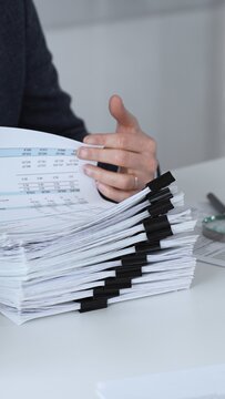Businessman analyzing financial documents and preparing reports, performing audit work in the office with a stack of paperwork, calculator, magnifying glass, and laptop. Audit and taxes