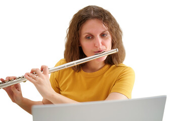 Woman musician playing silver flute while looking at laptop screen. Professional flutist learning musical composition online. Concept of virtual music lesson and remote hobby education. © Андрей Журавлев