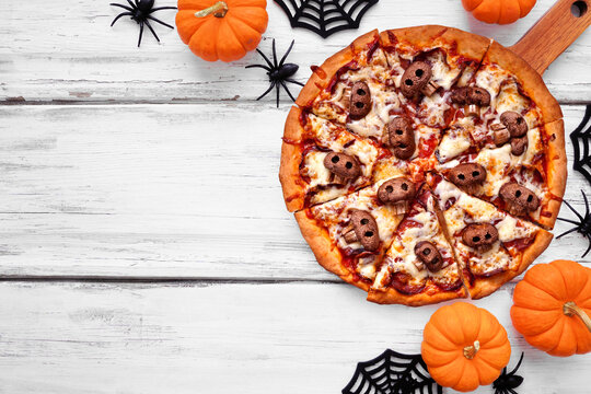 Halloween skull pizza. Top down view table scene on a white wood background. Pepperoni and cheese with spooky mushroom skulls. Copy space.
