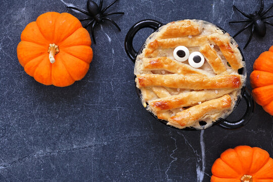 Halloween mummy chicken pot pie. Overhead view table scene on a dark stone background. Copy space.
