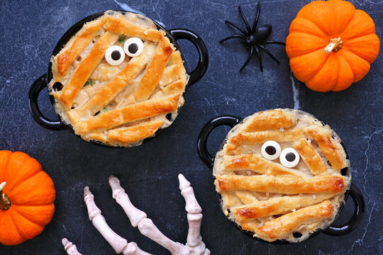 Halloween mummy chicken pot pies. Top down view table scene on a dark stone background.