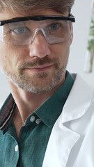 Adult male scientist in a lab coat and gloves examining a plant sample in a test tube, with a...