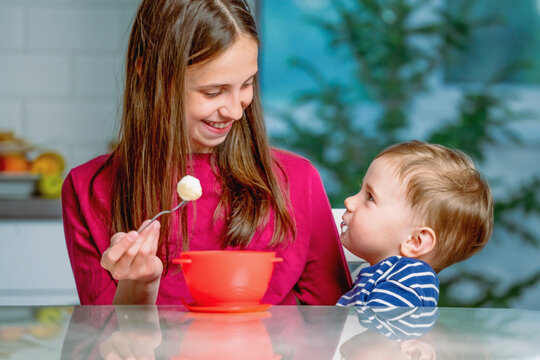 Older sister patiently feeding her toddler brother at home.