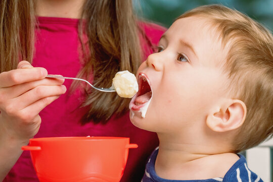 Girl feeding her younger brother from a bowl with a spoon.