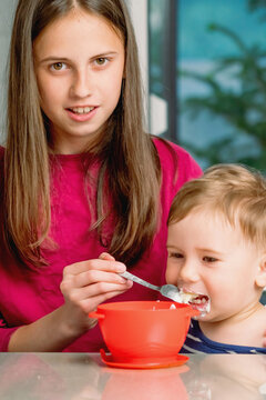 Caring sister feeding her toddler brother during a family meal.
