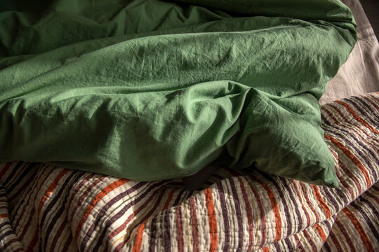An unassembled bed in the bedroom, a blanket, and green and beige bedding.