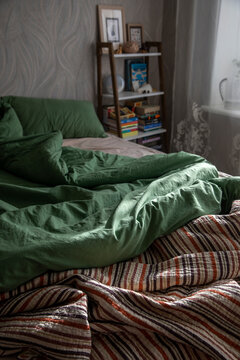 An unassembled bed in the bedroom, a blanket, and green and beige bedding.