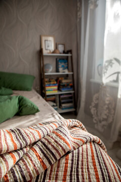 An unassembled bed in the bedroom, a blanket, and green and beige bedding.