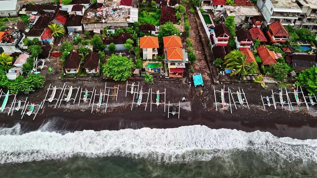 Aerial view of Amed Beach with traditional outrigger fishing boats lined up on the dark volcanic sand shore, Bali, Indonesia.