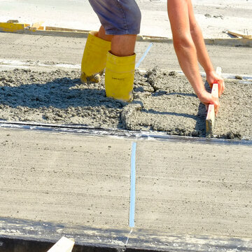 Worker smoothing wet concrete with a hand tool