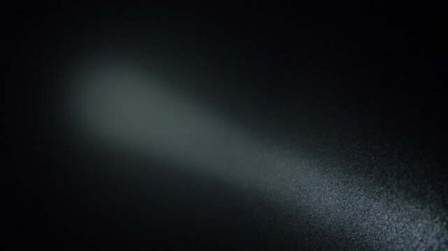 Strong light ray pierces darkness over residential area. Flashlight points skyward during silent night