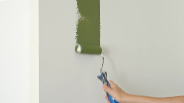 Woman painting interior wall green with a roller at home. DIY decorating and changing wall color during room makeover