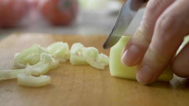 Bell pepper sliced into pieces by hostess, knife guiding through in preparation for family meal. Slices rest on wooden board surface. Home kitchen vibe. Food preparation scene. Chopping capsicum