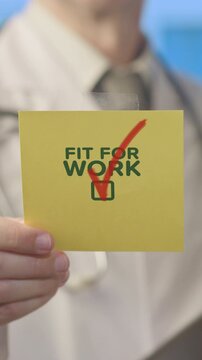 Medical professional in a white coat showing a sticky note with the text fit for work and a red checkmark, symbolizing a positive health assessment and readiness to resume employment
