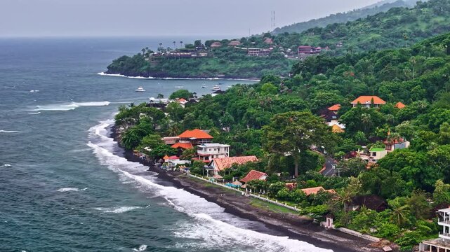 Aerial view of Amed Beach with its distinctive black sand, lush tropical hills, and coastal villas along the shoreline in Bali, Indonesia.