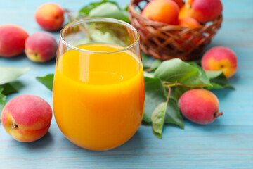 Apricot juice in glass, fresh fruits and leaves on light blue wooden table, closeup © New Africa