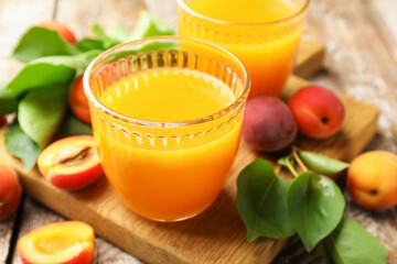 Glasses of tasty apricot juice, fresh fruits and leaves on wooden table, closeup © New Africa