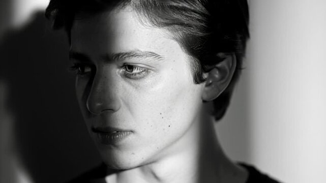 Shifting shaft of light revealing man turning head and glancing left in studio, dark shirt, pensive