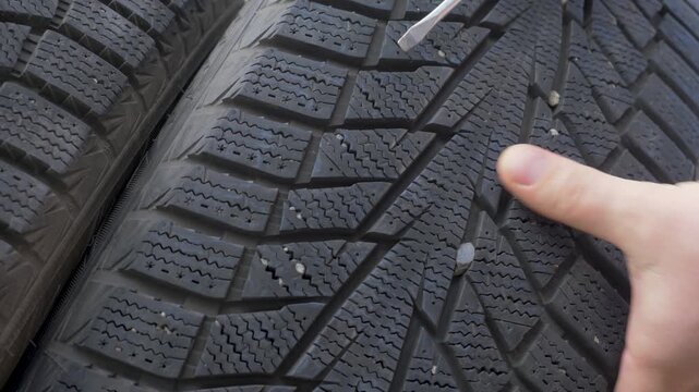 Mechanic hand takes out gravel stuck in rubber channels. Preparation before cold season ensures safety. Winter tread works best when free from stones and dirt