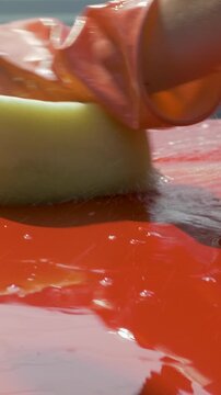 Driver uses yellow sponge to remove dirt from red car hood. Water cleanses surface, leaving a smooth finish. Emphasizes importance of keeping car exterior in excellent condition