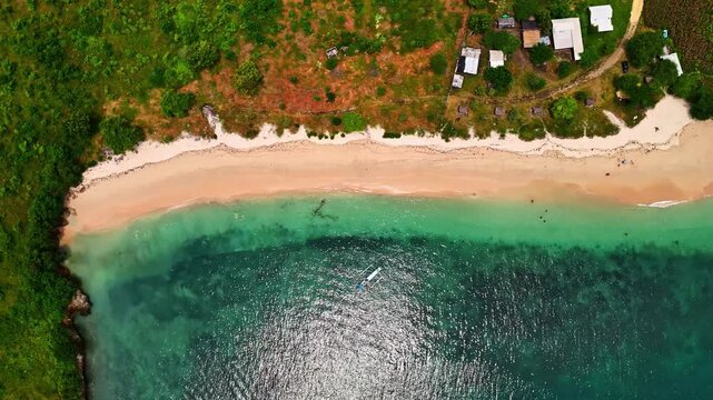 Aerial view of Kuta Beach with turquoise water, white sand, and a small boat floating in the sea in Kuta, Bali, Indonesia.