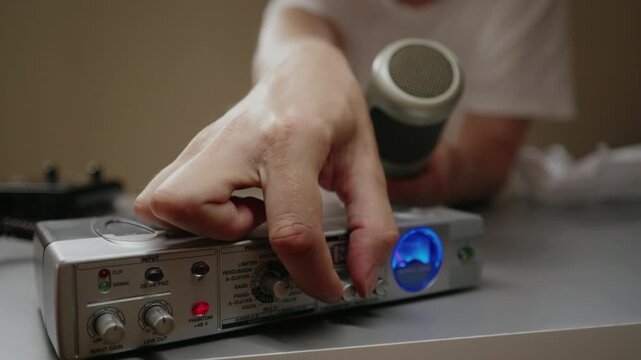Audio engineer turning knobs on vintage microphone preamp for sound recording. Concept of professional music production and equipment operation in recording studio setting, close-up, slow motion.