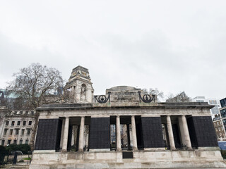 Obraz premium Urban war Tower Hill Memorial in London, UK with classical columns and pedestrians walking past on cloudy day. The Mercantile Marine Memorial.