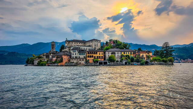 Panoramic view of San Giulio Island on Lake Orta during a golden hour and sunset, Piedmont, Italy, featuring the historic basilica and picturesque lakeside scenery surrounded by Alpine landscapes