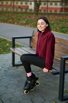 Woman seated in rollerblades on wooden bench, smiling to camera in burgundy fleece and black leggings. Suitable for sport, lifestyle branding, confidence or weekend activity themes