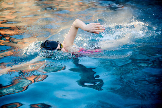 Female swimmer performing freestyle in outdoor pool, dynamic side view with vivid reflections and splashing water. Concept of determination, rhythm and active lifestyle