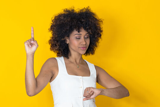 African American woman pointing finger up with an idea while checking the time on her wrist, isolated on yellow background
