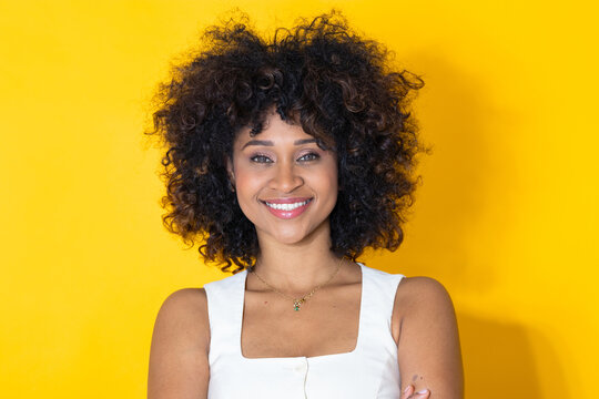 smiling hispanic latin woman with a bright, confident expression, arms crossed, posing against a vivid yellow studio background