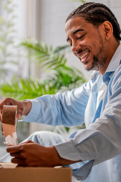 Smiling Black man taping cardboard box while packing for moving day at home