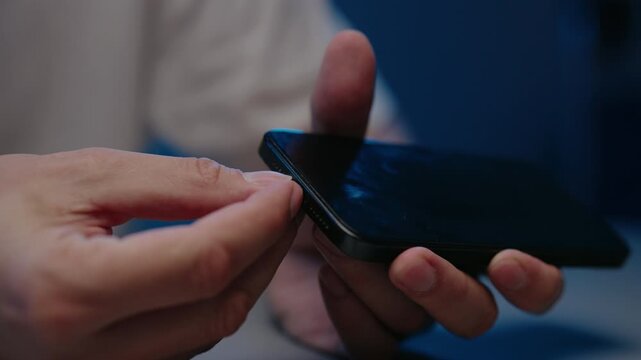 Closeup of hands removing black dust plug from smartphone charging port in dark room, blue lighting creating modern, tech focused atmosphere. Concept of phone care and accessory using.