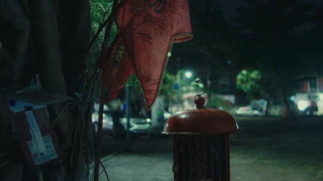 Red shrine and flag beside tree at night in quiet urban park with streetlights
