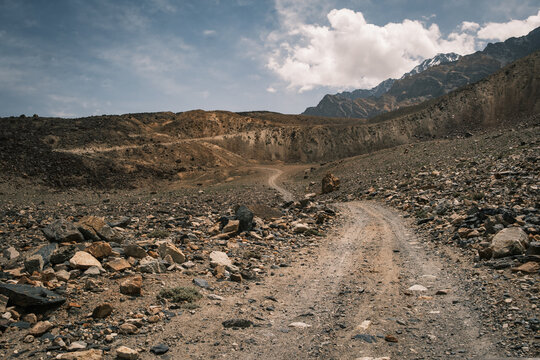 View of the rugged, unpaved road winding through the arid, rocky landscape of the Bartang valley, with mountains in the background in Chah Ab, Gorno-Badakhshan, Tajikistan.