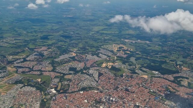 Aerial view from a passenger plane over S&atilde;o Paulo State, Brazil, revealing a diverse landscape of dense urban areas, winding road networks, green spaces and agricultural land below
