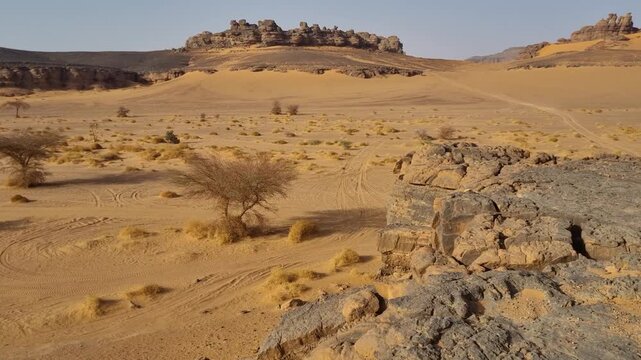 Saharan sandy landscape weave between rugged rock formations under a clear sunny sky, revealing an immense desert wilderness with a striking sense of remoteness and solitude, Djanet, Algeria