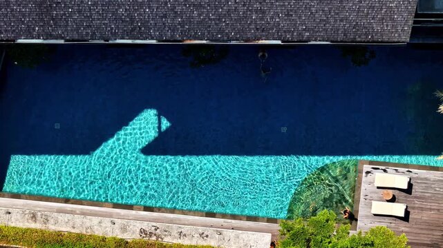 Aerial view of a swimming pool with clear blue water and wooden deck in a modern villa in Kecamatan Kuta Utara, Bali, Indonesia.