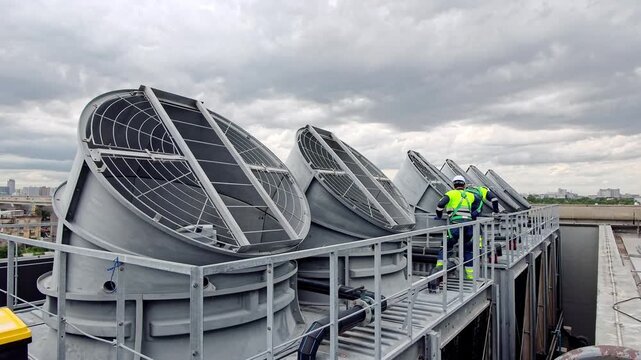 Workers perform maintenance on rooftop cooling units in a city