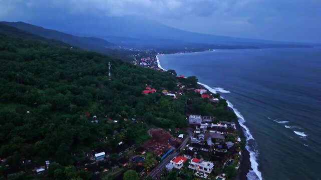 Aerial view of Amed Beach with lush green hills, coastal road, and buildings along the shoreline in Bali, Indonesia.