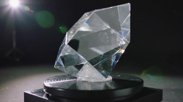 Rotating turntable moving faceted crystal on black base, revealing rainbow highlights by left light