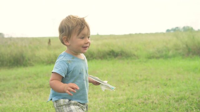 Toddler running into open field with paper airplane and arm raised