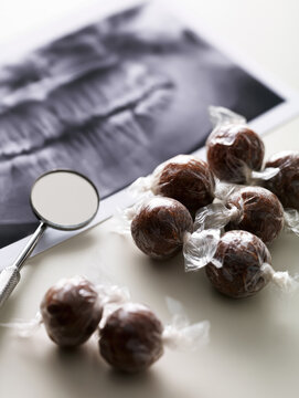 Dental X ray, mouth mirror, and wrapped chocolate candy create clinical still life with spooky tooth checkup mood, soft daylight, tactile texture, and clean copy space for dental care concepts