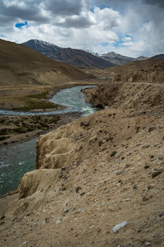 View of the Wakhan Corridor with a winding river flowing through rugged mountains, rocky slopes, and snow-capped peaks in Badakhshan, Afghanistan.
