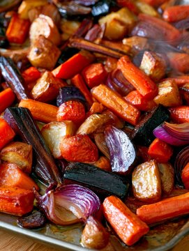 Roasted root vegetables and red onions simmering on a baking sheet