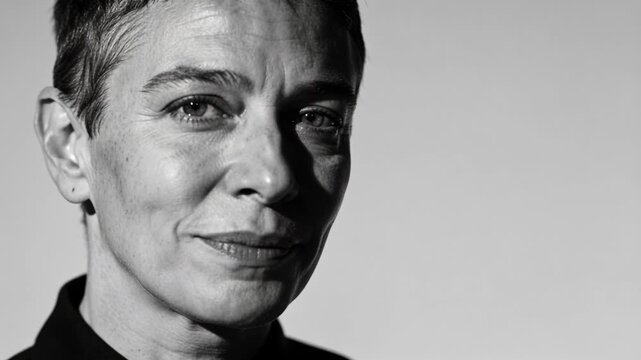 Turning woman in dark collared top posing in studio, camera starting, showing earring under light