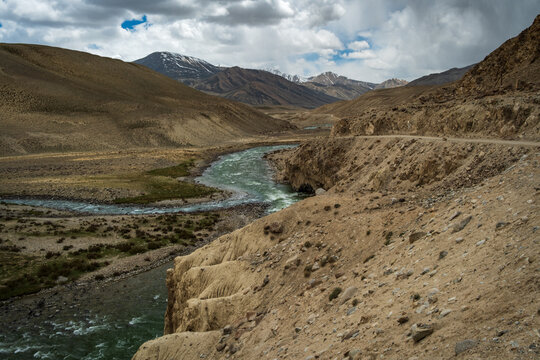 View of the Wakhan Corridor with a winding river flowing through arid mountainous terrain under a cloudy sky in Badakhshan, Afghanistan.
