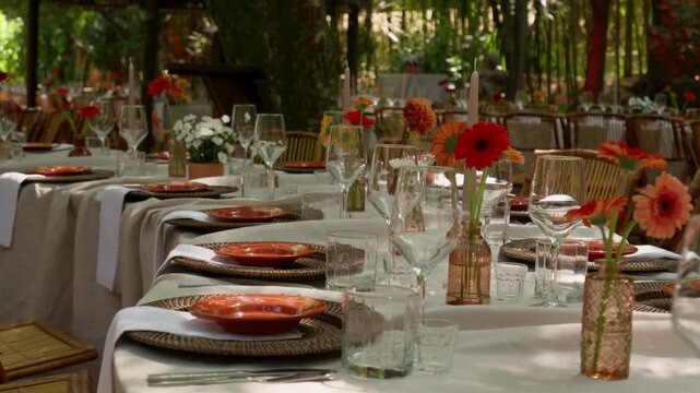 Garden table set with orange gerberas amber vases wine glasses and woven placemats